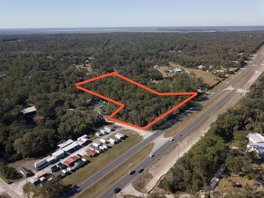 An aerial view shows a wooded lot outlined in red adjacent to a multi-lane highway — N US HWY 17, DELAND, FL