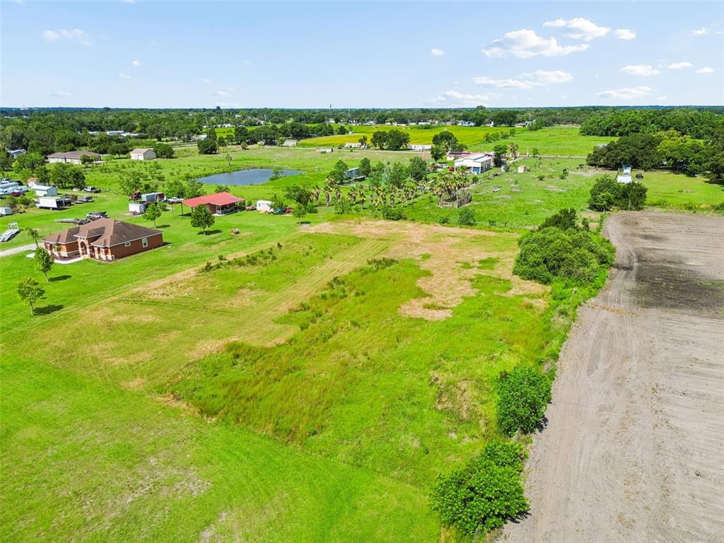 An aerial view shows a large, grassy vacant lot adjacent to a house and dirt road — 0 KILLEYMOON LANE, DOVER, FL