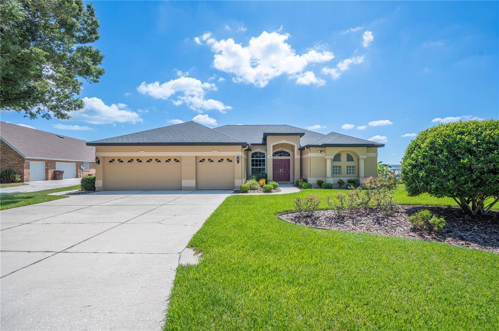 A single-story house with a three-car garage, tan stucco exterior, and a large front lawn — 102 BAYBERRY DRIVE, POLK CITY, FL