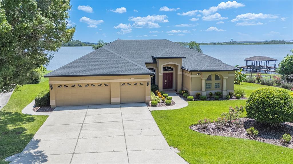 A tan single-story house with a three-car garage sits on a lakefront lot — 102 BAYBERRY DRIVE, POLK CITY, FL