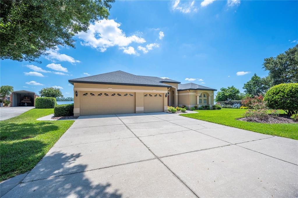 A tan single-story house with a three-car garage and a large concrete driveway — 102 BAYBERRY DRIVE, POLK CITY, FL