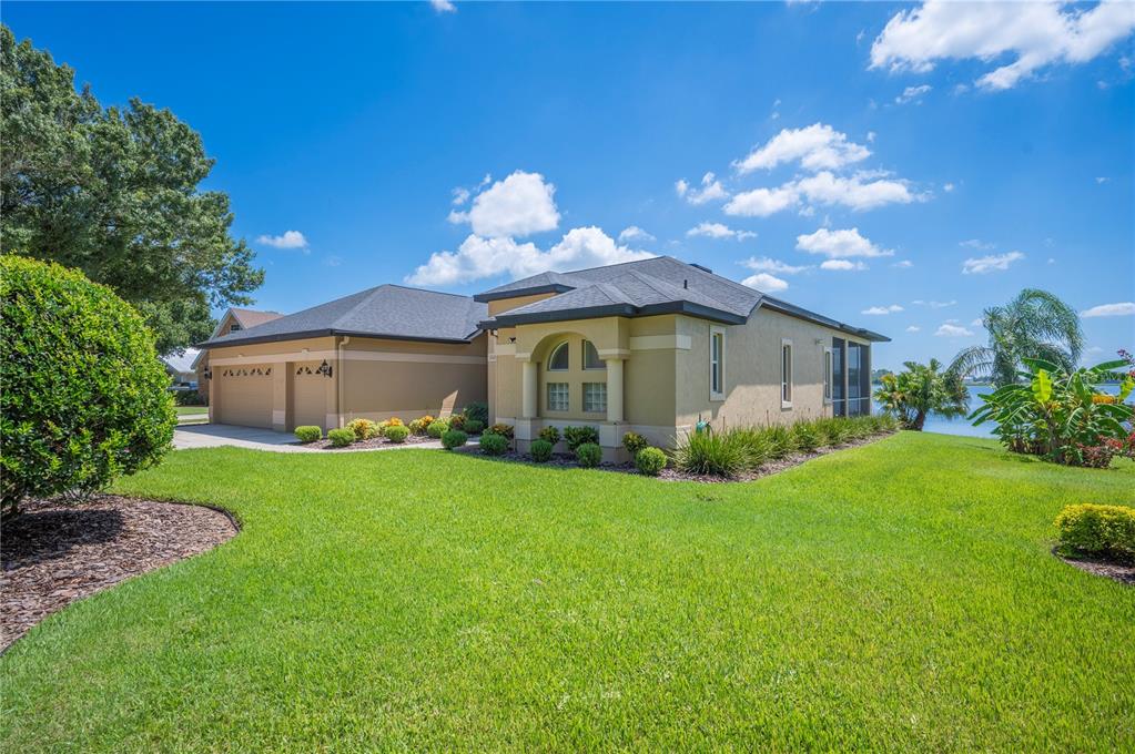 A tan single-story house with a two-car garage and a screened lanai overlooking a lake — 102 BAYBERRY DRIVE, POLK CITY, FL