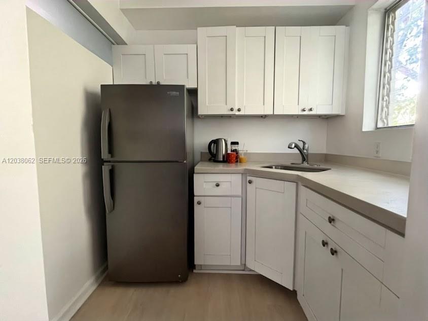 A small kitchen features white cabinets, a stainless steel refrigerator, and a corner sink — 1027 Euclid Ave # 5, Miami Beach FL 33139, MIAMI BEACH, FL