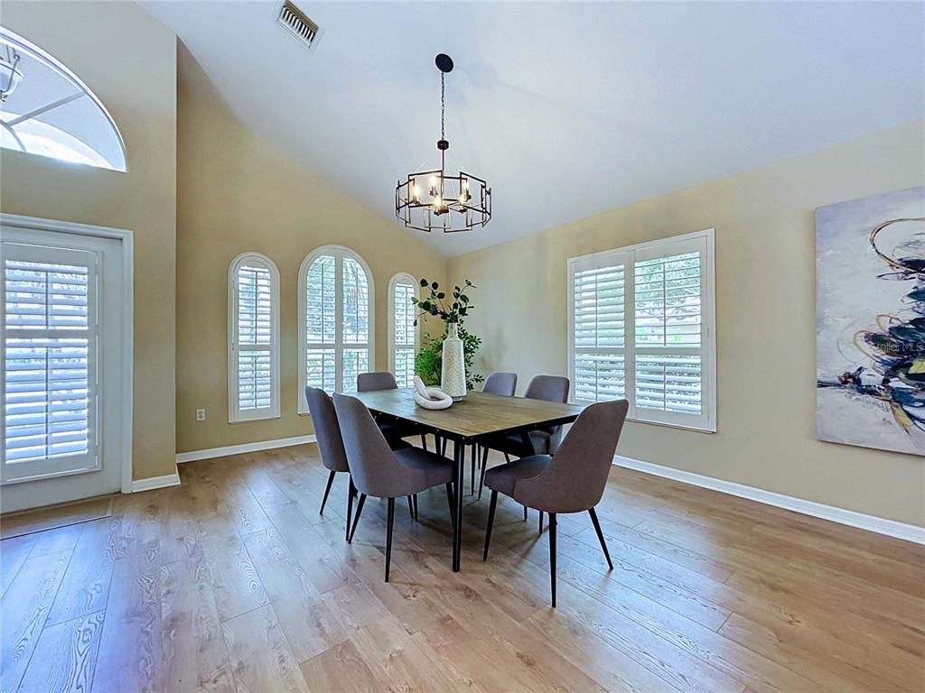 A dining room features a wooden table, six gray chairs, a chandelier, and arched windows — 7703 BRITISH OPEN WAY, LAKEWOOD RANCH, FL