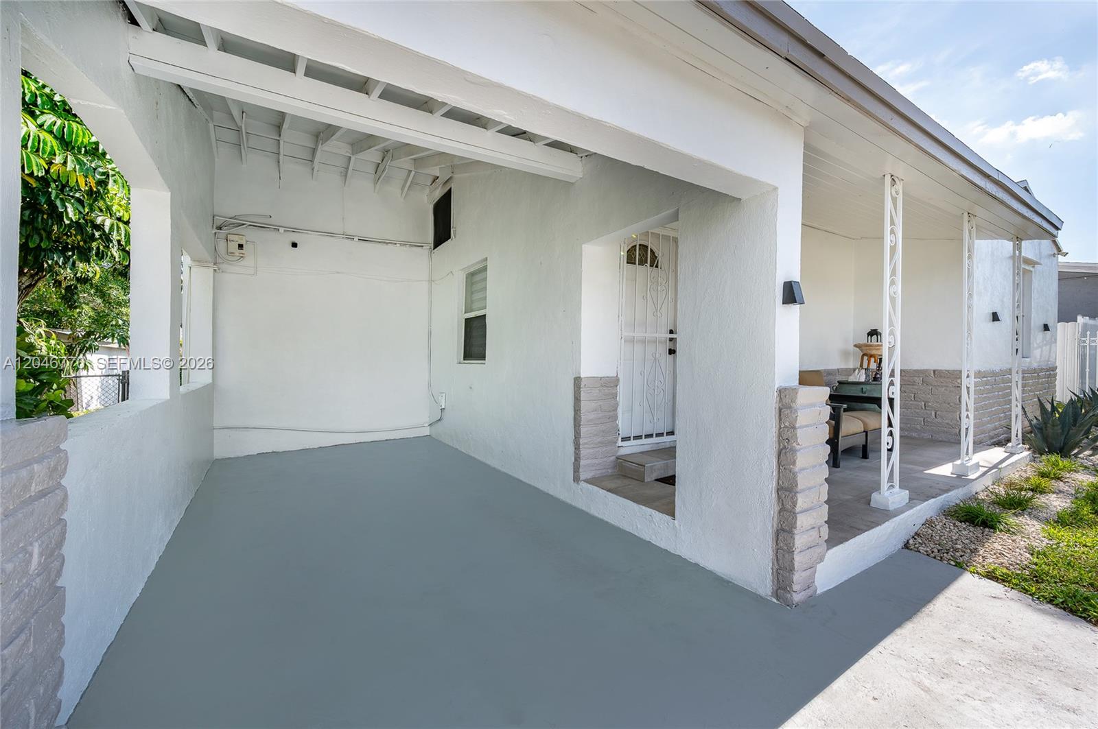 A covered concrete patio features white stucco walls, brick accents, and decorative metal porch columns — 2371 NW 85th St, Miami FL 33147, MIAMI, FL