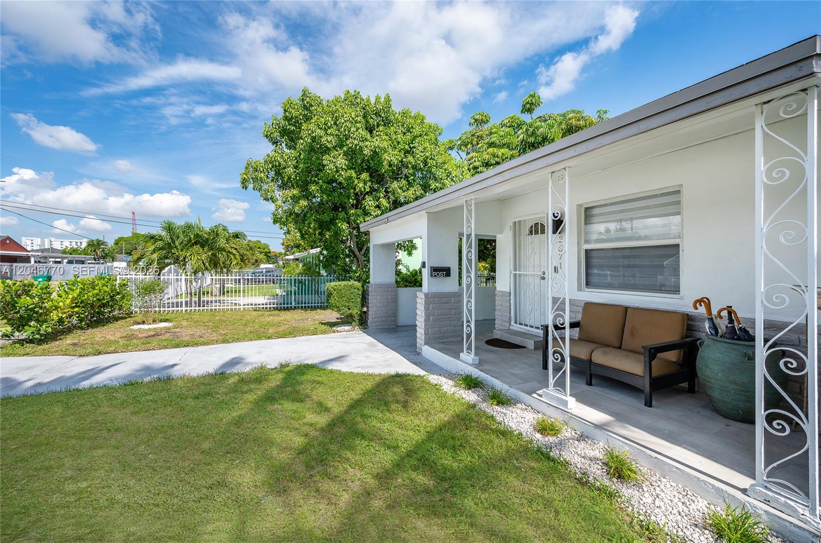 A white house features a covered front porch with decorative metal columns and a sofa — 2371 NW 85th St, Miami FL 33147, MIAMI, FL