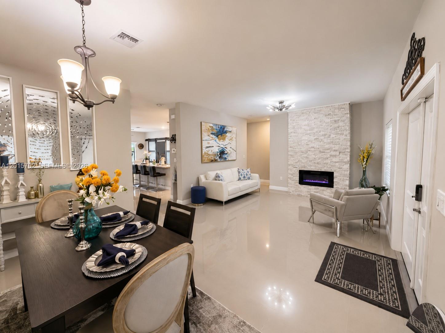 An open-concept living and dining area features a stone fireplace, tile floors, and modern decor — 21480 SW 132nd Ct, Miami FL 33177, MIAMI, FL