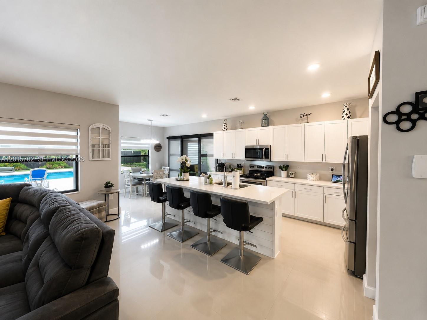 A modern kitchen features white cabinetry, a central island with bar seating, and tile flooring — 21480 SW 132nd Ct, Miami FL 33177, MIAMI, FL