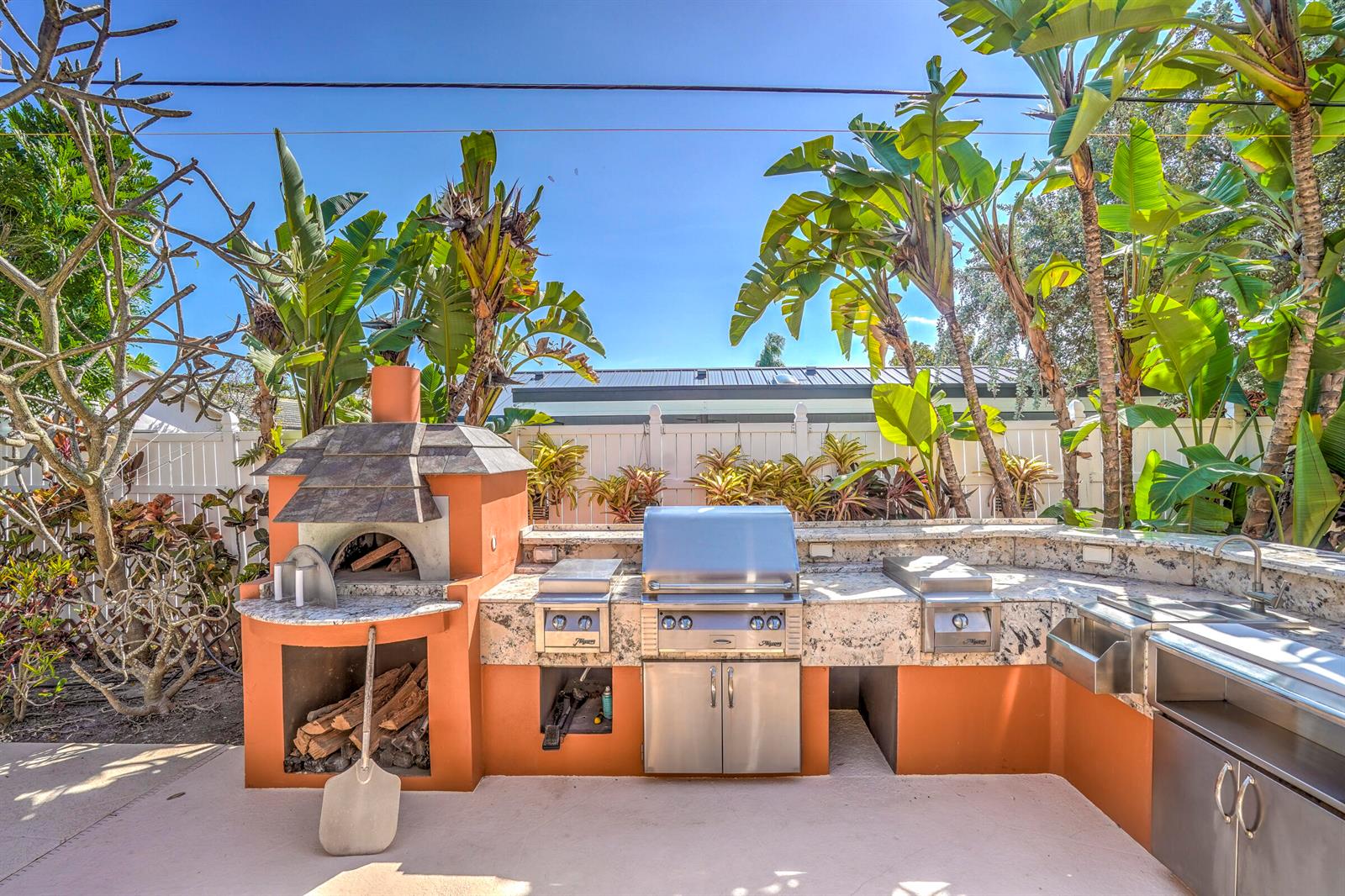 An outdoor kitchen features a wood-fired pizza oven, stainless steel grill, and granite countertops — 1191 Emerald Lane, Singer Island FL 33404, SINGER ISLAND, FL