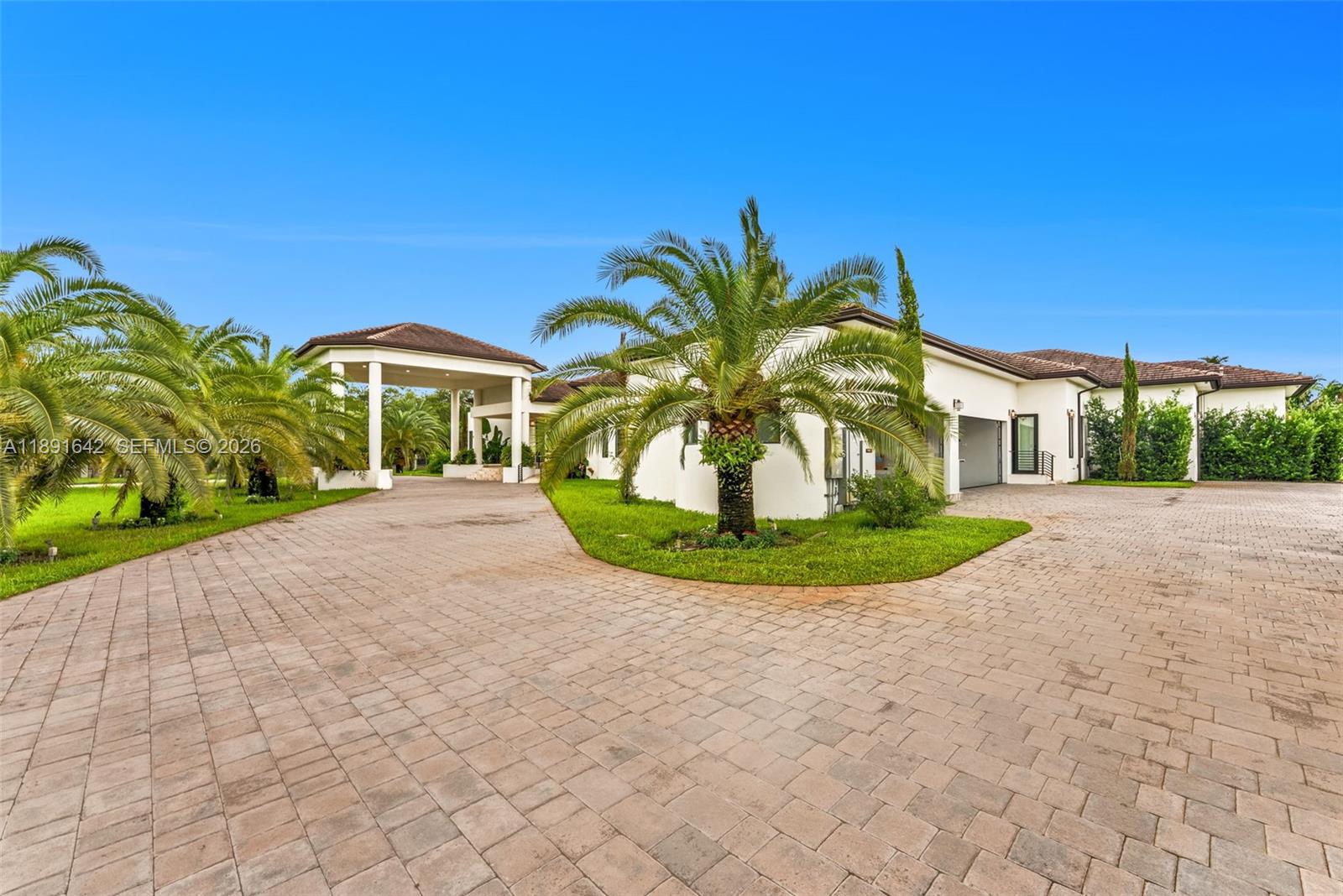 A paved driveway leads to a white house with a porte-cochère and palm trees — 12175 SW 45th St, Miami FL 33175, MIAMI, FL