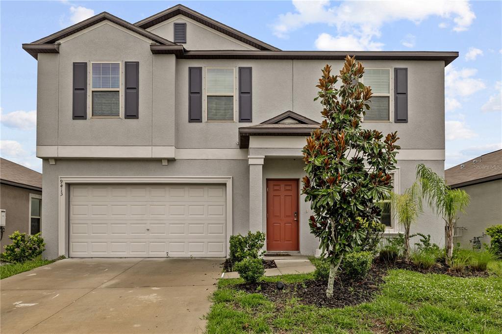 A two-story suburban house with a gray stucco exterior, a two-car garage, and red door — 9413 CHANNING HILL DRIVE, RUSKIN, FL