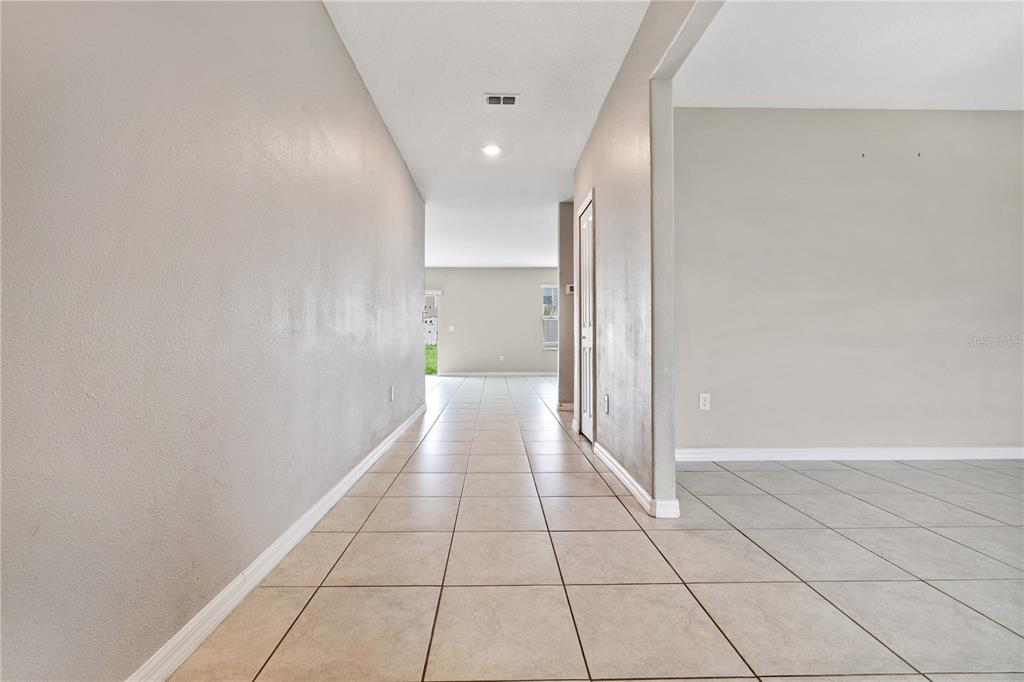 A tiled hallway leads from the foreground toward an open living area with large windows — 9413 CHANNING HILL DRIVE, RUSKIN, FL