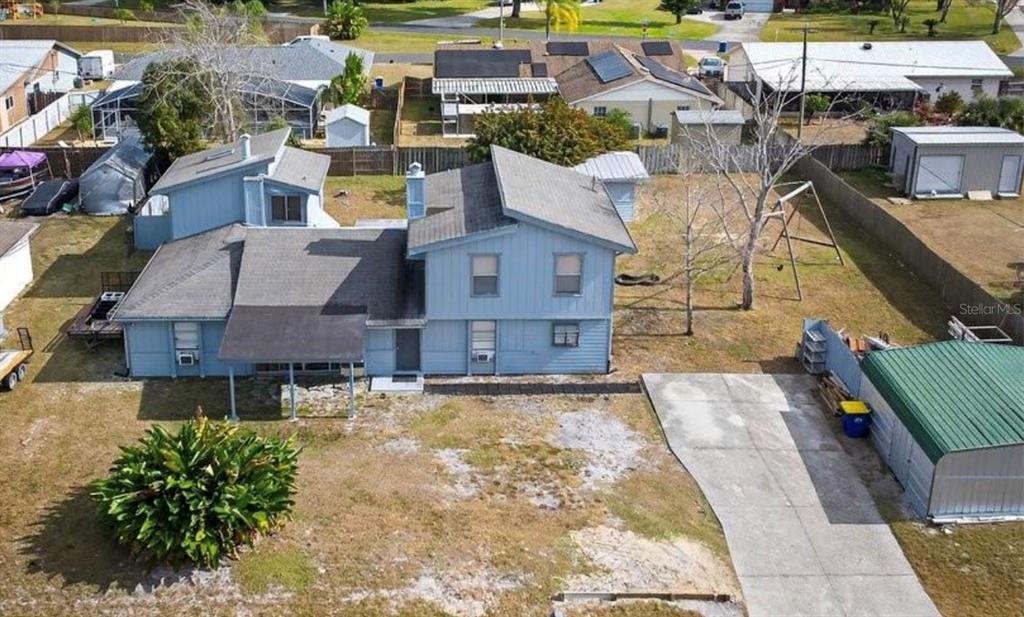 An aerial view shows a two-story blue house with a metal carport and backyard swing set — 2519 FERN PALM DRIVE, EDGEWATER, FL