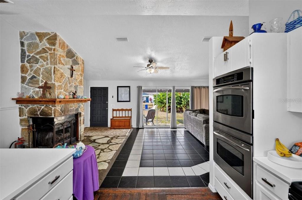A kitchen and living area featuring a stone fireplace, black tile flooring, and double wall ovens — 2519 FERN PALM DRIVE, EDGEWATER, FL