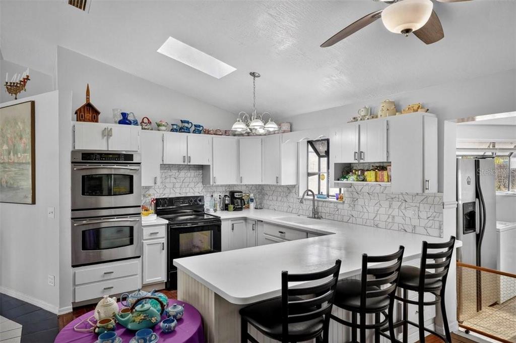 A kitchen features white cabinets, stainless steel appliances, a breakfast bar, and a marble backsplash — 2519 FERN PALM DRIVE, EDGEWATER, FL
