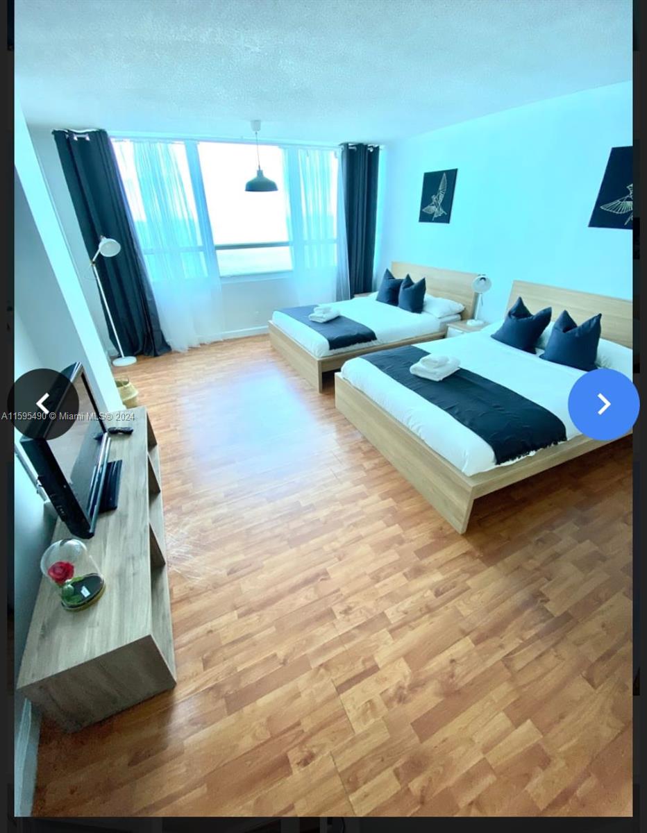 A bedroom features two beds, wood-look flooring, and large windows with dark curtains — 5445 Collins Ave # 1735, Miami Beach FL 33140, MIAMI BEACH, FL