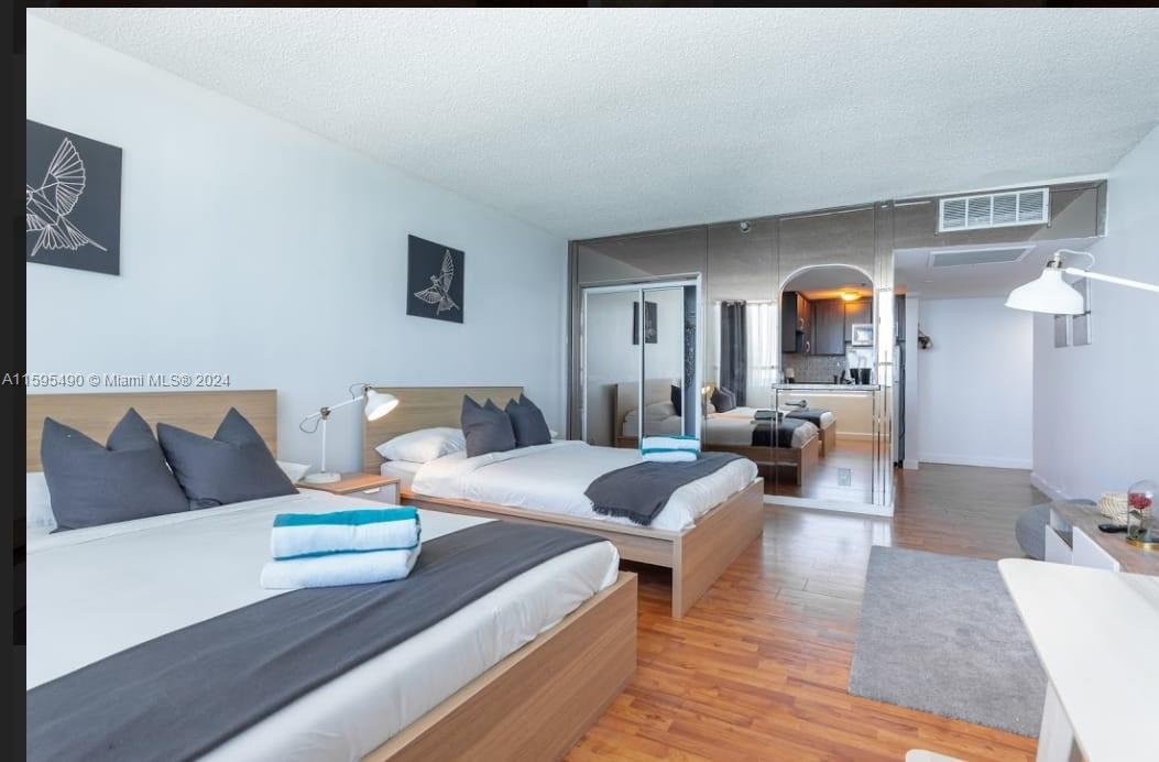 A bedroom with two beds, wood-look flooring, and a mirrored wall reflecting a kitchen area — 5445 Collins Ave # 1735, Miami Beach FL 33140, MIAMI BEACH, FL