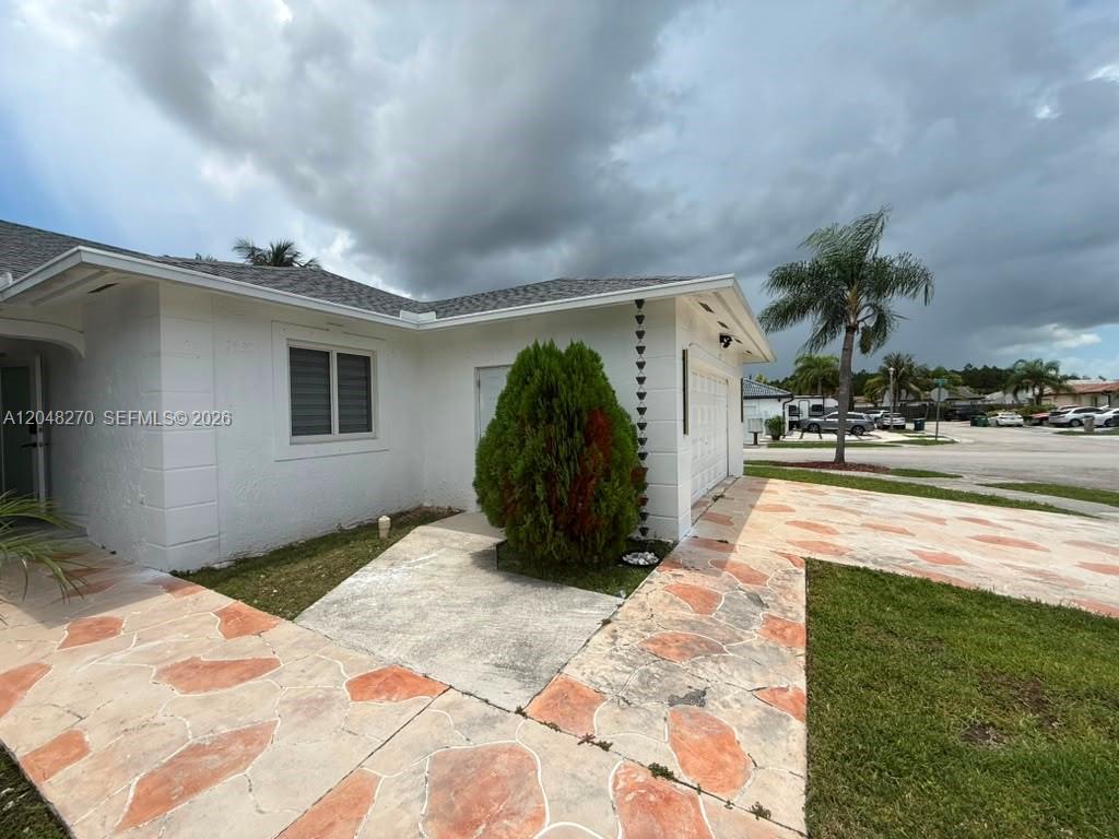 A white house exterior features a stone-patterned walkway and a large evergreen shrub — 14305 SW 182nd Ter # 0, Miami FL 33177, MIAMI, FL