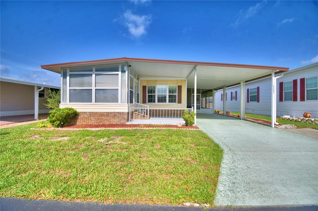 A single-story manufactured home with a carport, brick skirting, and a front-facing sunroom — 4807 PLUMWOOD STREET, WINTER HAVEN, FL