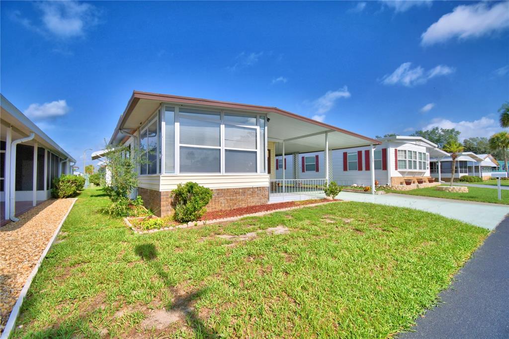 A single-story manufactured home with a brick base, large windows, and an attached carport — 4807 PLUMWOOD STREET, WINTER HAVEN, FL