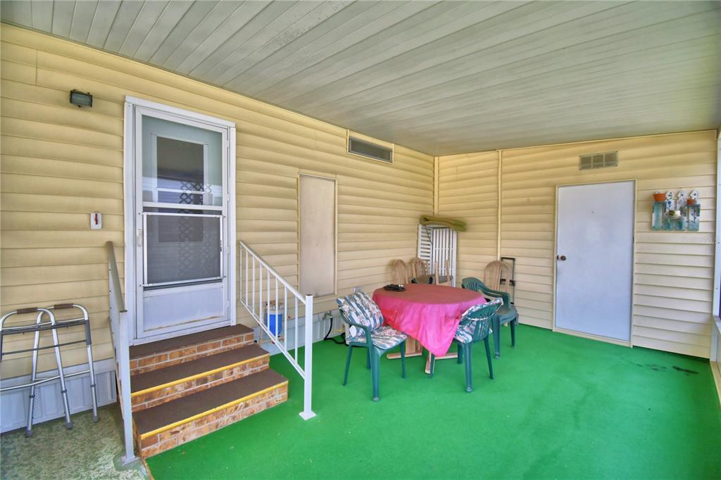 A covered porch with yellow siding, green flooring, a table with chairs, and two doors — 4807 PLUMWOOD STREET, WINTER HAVEN, FL