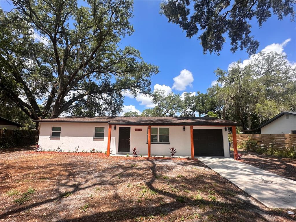 A single-story house with a white exterior, dark garage door, and wooden porch supports — 14808 N 30TH STREET, LUTZ, FL
