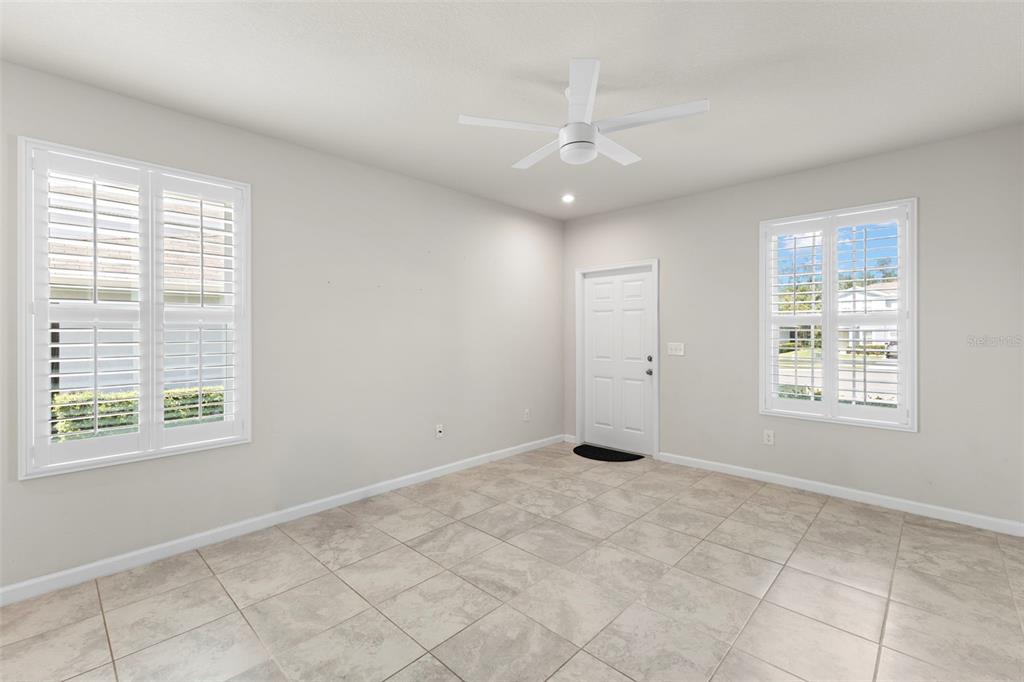 An empty room with light-colored tile flooring, white walls, plantation shutters, and a ceiling fan — 3150 VICTORIA INLET DRIVE, HOLIDAY, FL
