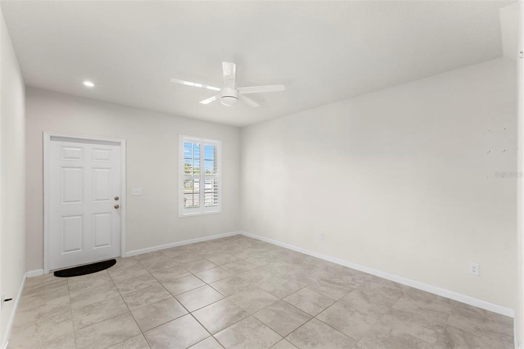 An empty room with light-colored tile flooring, a white ceiling fan, and a white door — 3150 VICTORIA INLET DRIVE, HOLIDAY, FL
