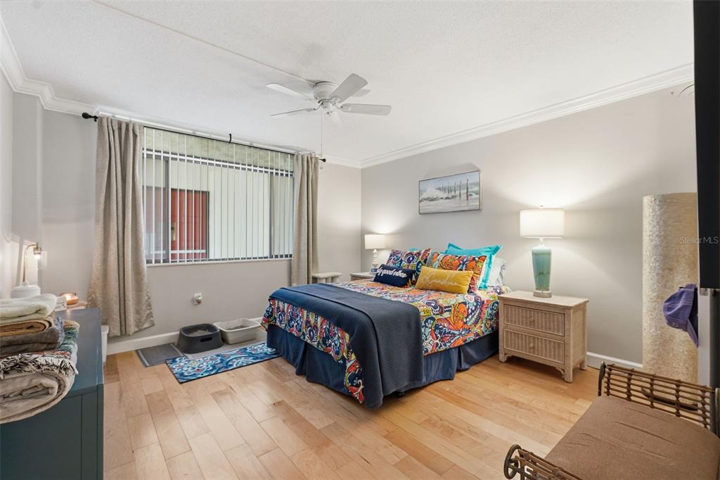 A bedroom features hardwood floors, a ceiling fan, a queen bed, and a window with curtains — 2612 PEARCE DRIVE UNIT 211, CLEARWATER, FL