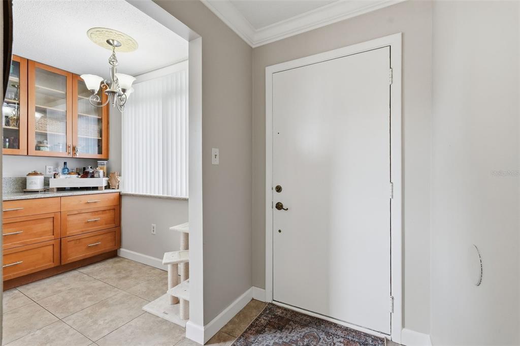 An entryway with a white door leads into a kitchen area featuring wooden cabinetry — 2612 PEARCE DRIVE UNIT 211, CLEARWATER, FL