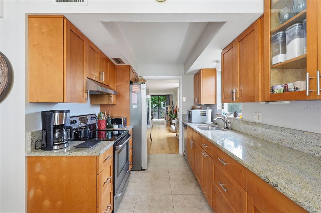 A galley kitchen features light wood cabinets, granite countertops, and stainless steel appliances — 2612 PEARCE DRIVE UNIT 211, CLEARWATER, FL