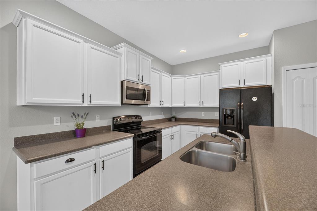 A kitchen features white cabinets, dark countertops, a black microwave, and a black refrigerator — 2637 WALDEN WOODS DRIVE, PLANT CITY, FL