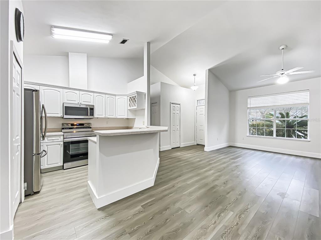 A kitchen with white cabinets and stainless steel appliances opens to a living area — 10301 SW 52ND AVENUE, GAINESVILLE, FL