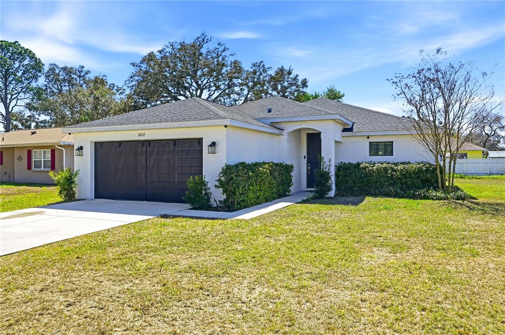 A single-story house with a white exterior, a dark garage door, and a front lawn — 8452 DORSEY STREET, SPRING HILL, FL