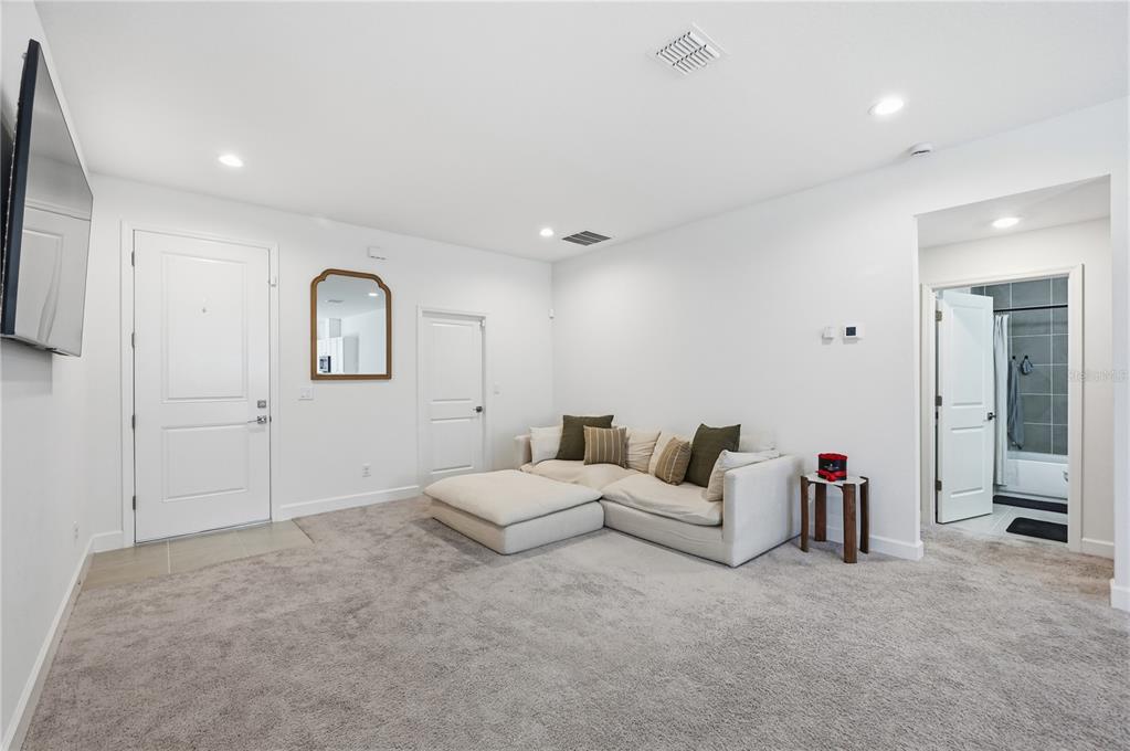 A carpeted living room features a white sectional sofa, a mirror, and a bathroom doorway — 8452 DORSEY STREET, SPRING HILL, FL