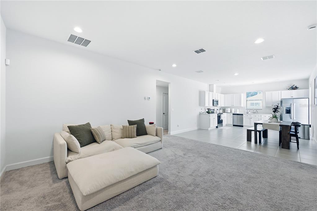 A living room with beige carpet and a sectional sofa opens to a tiled kitchen — 8452 DORSEY STREET, SPRING HILL, FL