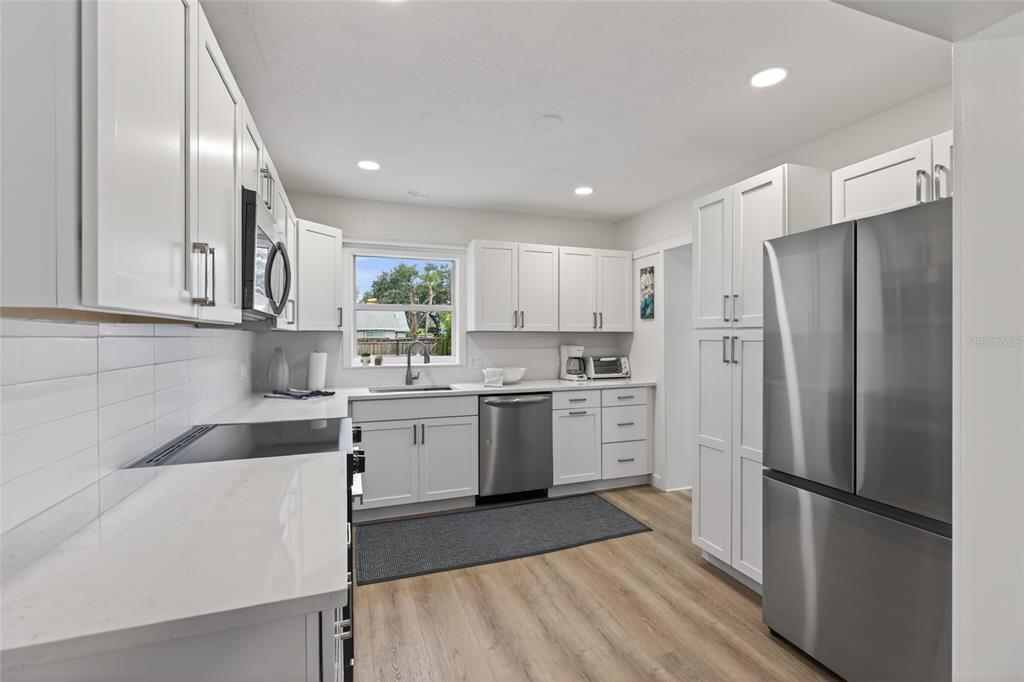 A modern kitchen features white cabinets, stainless steel appliances, light countertops, and wood-look flooring — 5617 19TH AVENUE S, ST PETERSBURG, FL