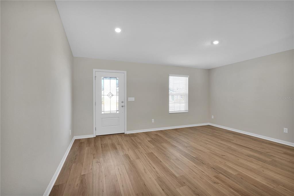 An empty living room features light gray walls, wood-look flooring, a white front door, and windows — 27 PRINCE KAAREL LANE, PALM COAST, FL