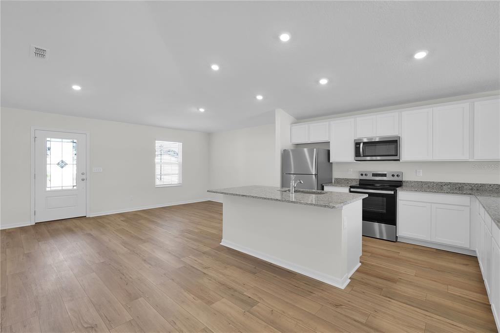 A kitchen with white cabinets, granite countertops, and stainless steel appliances opens to a living area — 27 PRINCE KAAREL LANE, PALM COAST, FL