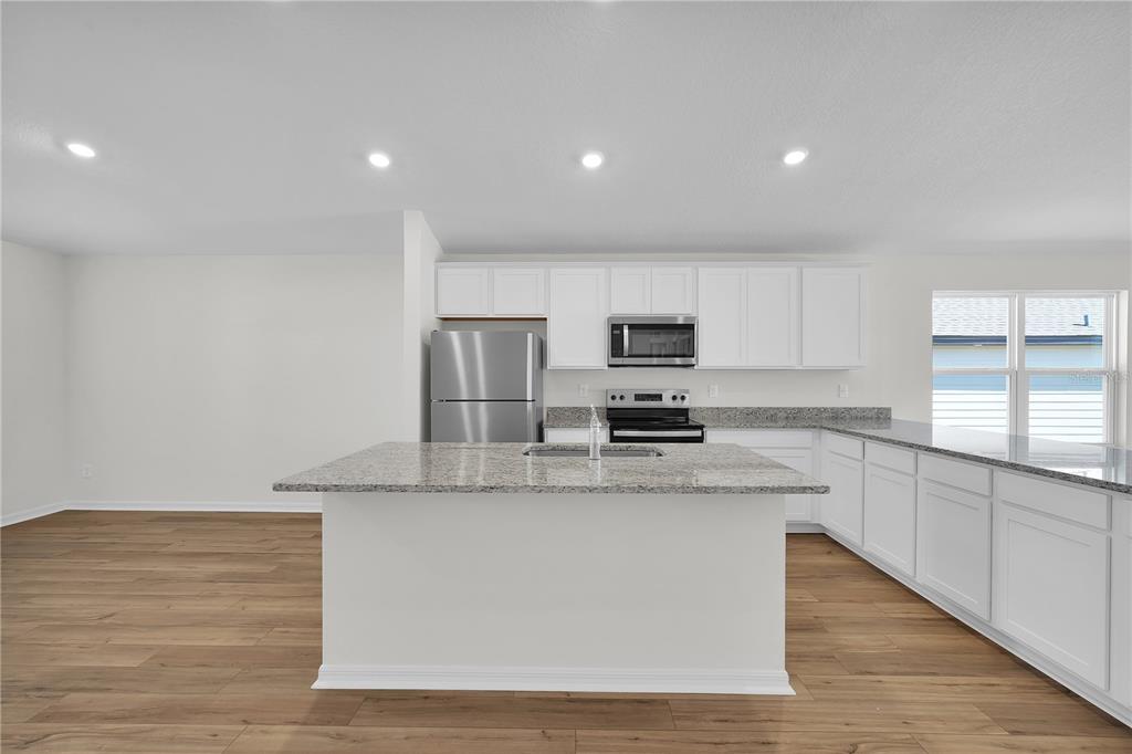 A kitchen with white cabinets, granite countertops, a center island, and wood-look flooring — 27 PRINCE KAAREL LANE, PALM COAST, FL