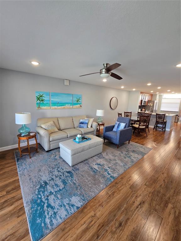 A living room with hardwood floors, a beige sofa, a blue armchair, and dining area — 7600 SUN ISLAND DRIVE S UNIT 306, SOUTH PASADENA, FL