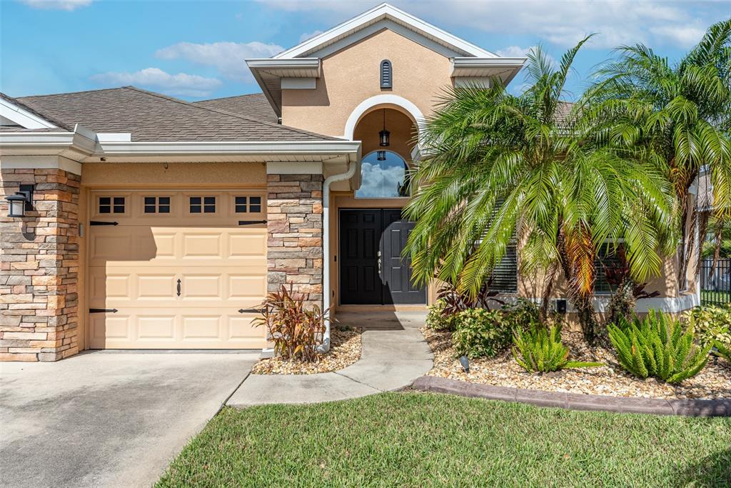 A single-story house with a tan stucco facade, stone accents, a garage, and a palm tree — 11236 77TH STREET E, PARRISH, FL