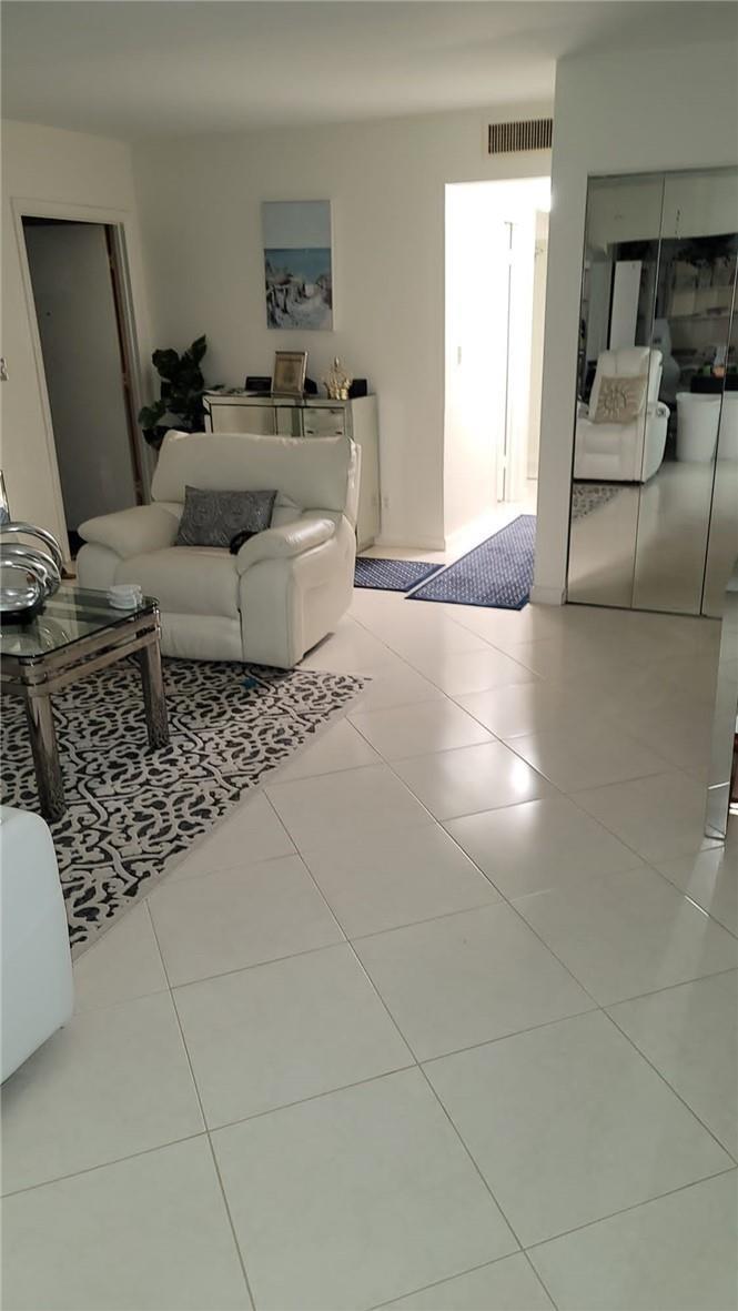 A living room with white tile floors, a white armchair, and a patterned area rug — 6574 Burning Wood Drive # 101, Boca Raton FL 33433, BOCA RATON, FL