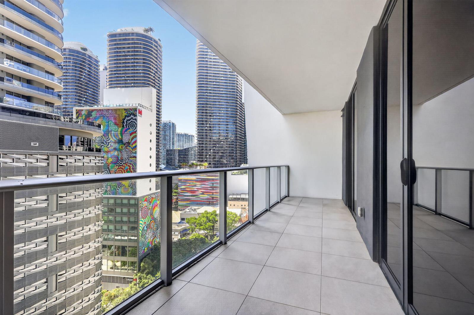 A modern balcony with tiled flooring and a glass railing overlooks a dense city skyline — 1010 Brickell Avenue # 1607, Miami FL 33131, MIAMI, FL