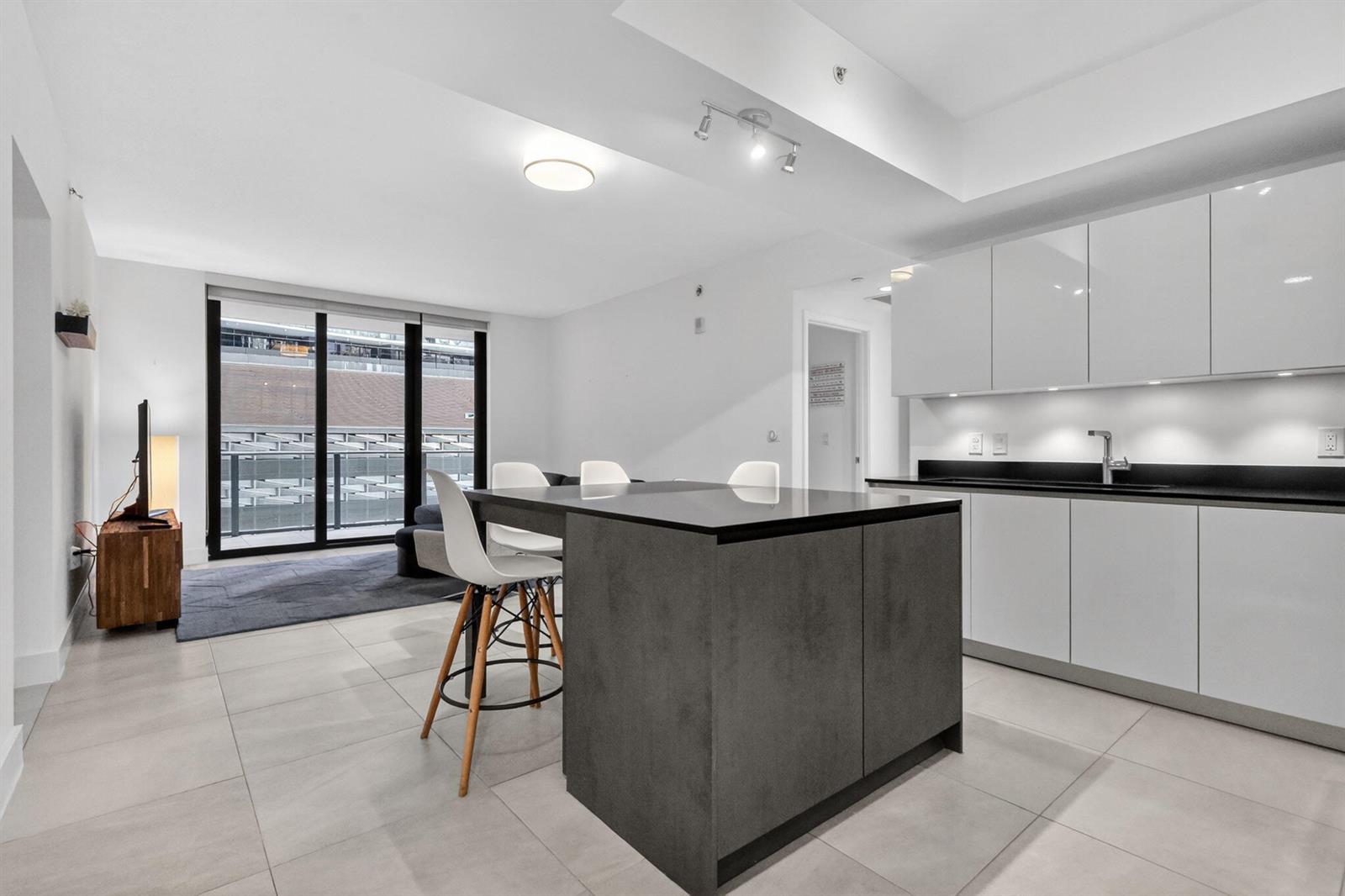 A modern kitchen with a dark island and white cabinets opens into a living area — 1010 Brickell Avenue # 1607, Miami FL 33131, MIAMI, FL