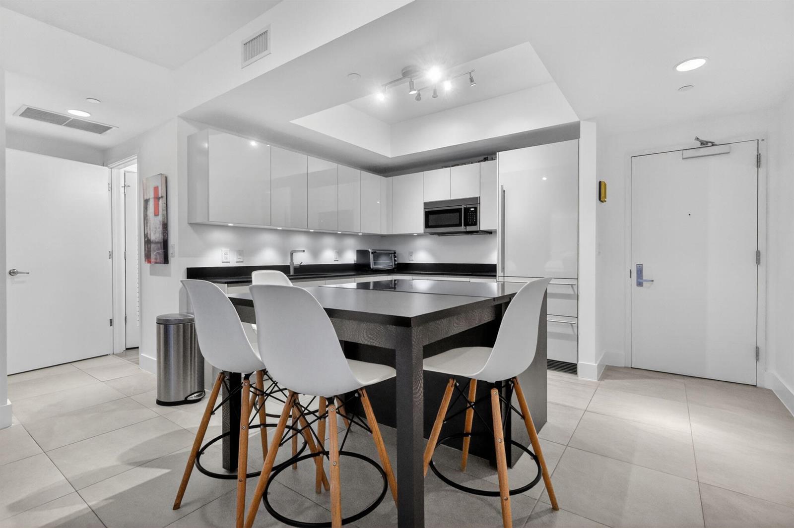 A modern kitchen features white cabinets, a black island with bar stools, and tiled floors — 1010 Brickell Avenue # 1607, Miami FL 33131, MIAMI, FL