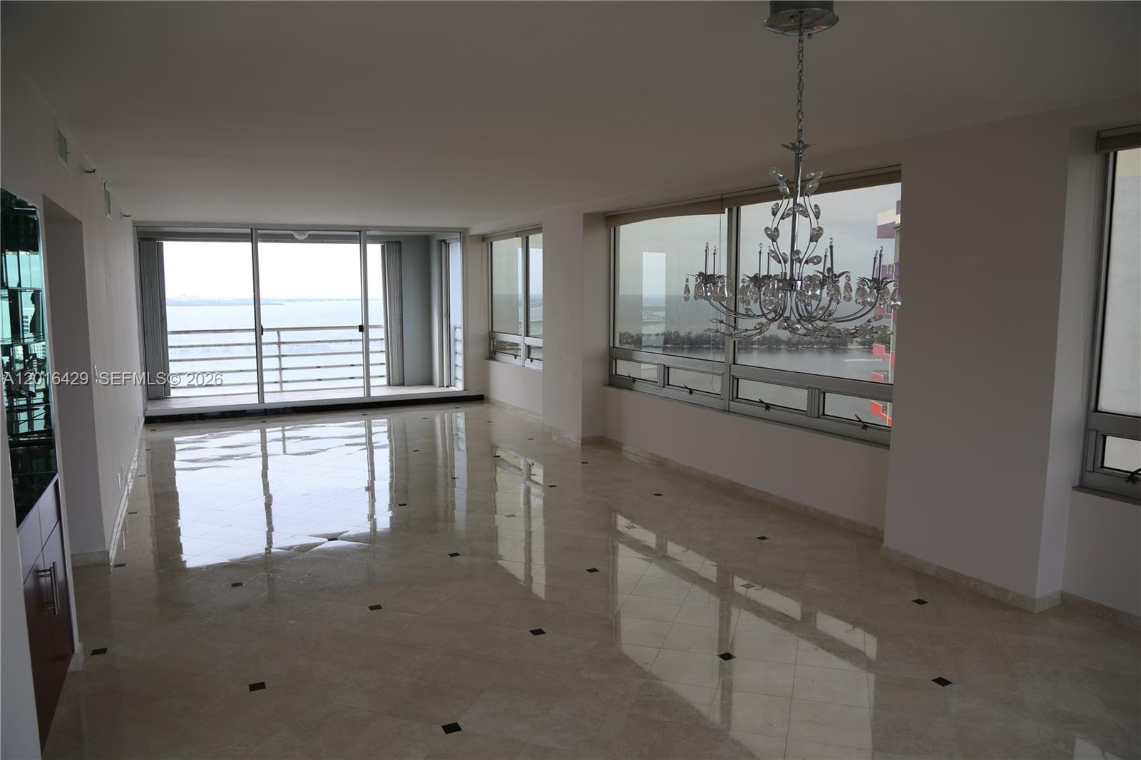An empty room features polished marble floors, a crystal chandelier, and large windows overlooking water — 1541 Brickell Ave # A3101, Miami FL 33129, MIAMI, FL