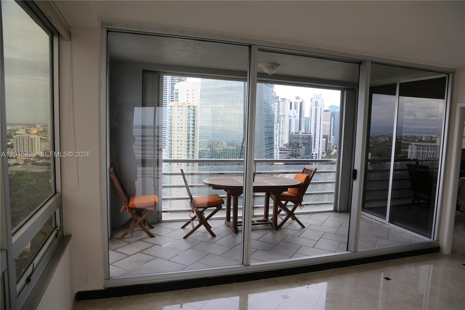 A balcony with a small wooden dining set overlooks a city skyline through glass doors — 1541 Brickell Ave # A3101, Miami FL 33129, MIAMI, FL