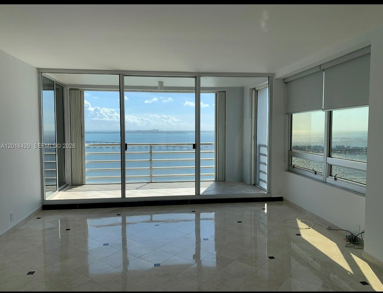 A bright, empty room features polished tile floors, floor-to-ceiling windows, and a balcony overlooking water — 1541 Brickell Ave # A3101, Miami FL 33129, MIAMI, FL