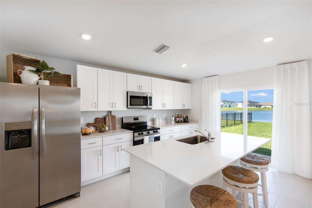 A modern kitchen features white cabinetry, stainless steel appliances, a quartz island, and water views — 11927 BROOKSIDE AVENUE, PORT CHARLOTTE, FL